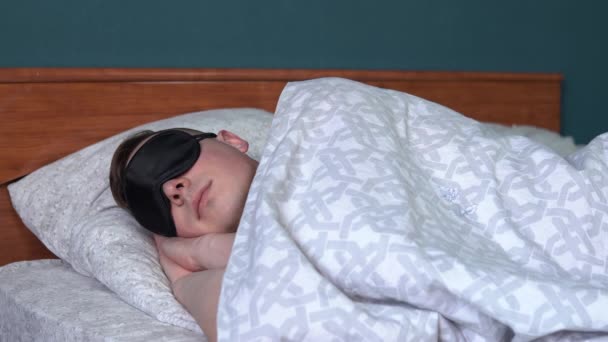 Ein junger Mann schläft in einer Schlafmaske. Ein Mann liegt im Bett in seinem Zimmer. — Stockvideo