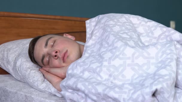 Молодой человек спит под одеялом. Мужчина лежит в постели в своей комнате . — стоковое видео