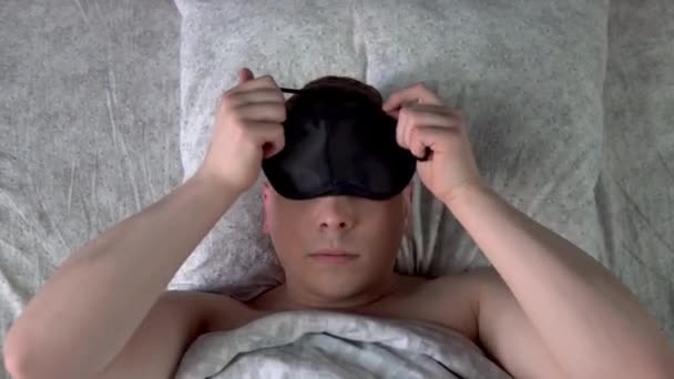 De jongeman gaat naar bed en doet een masker op. Een man ligt in bed in zijn kamer. Uitzicht van bovenaf. — Stockvideo