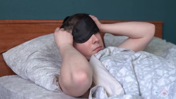 Ο νεαρός πάει για ύπνο και φοράει μάσκα. Ένας άντρας ξαπλώνει στο κρεβάτι του στο δωμάτιό του.. — Αρχείο Βίντεο