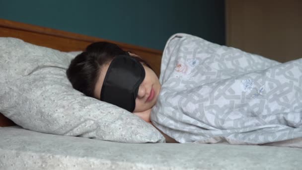 Mladá žena spí ve spánkové masce. Dívka leží v posteli v jeho pokoji. — Stock video