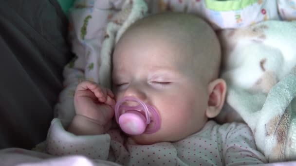 아기는 유모차를 타고 입 안에서 고무젖꼭지를 물고 자고 있다. 얼굴을 감아. — 비디오