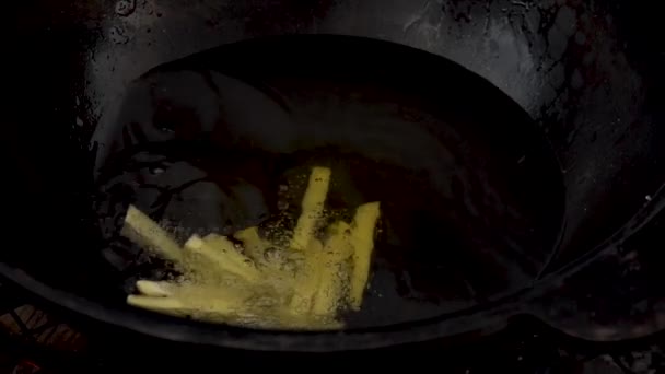 Een vrouw gooit aardappelen in een pot kokende olie. Gesneden aardappel kookt in olie close-up. Langzaam.. — Stockvideo