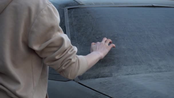 Una joven escribe con un dedo en un coche sucio "por favor lávame". Chica broma sobre el dueño del coche. El coche está cubierto de barro.. — Vídeo de stock