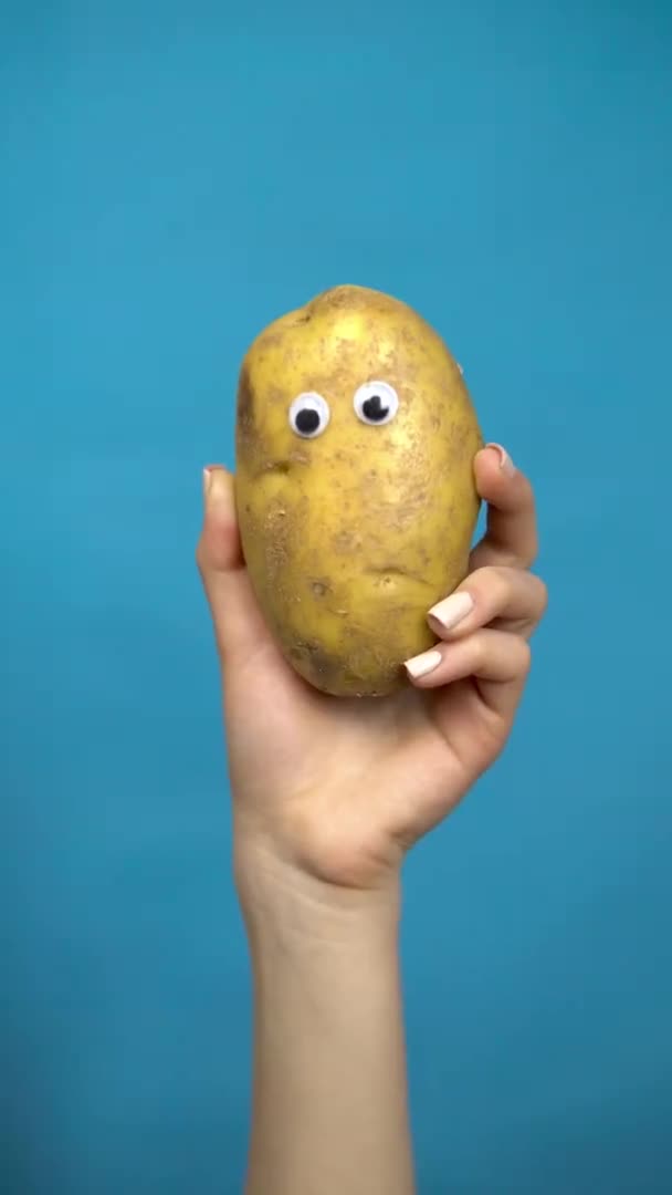 Occhi di patata in una mano di donna da vicino. Potatos si guarda intorno su uno sfondo blu. Video verticale . — Video Stock