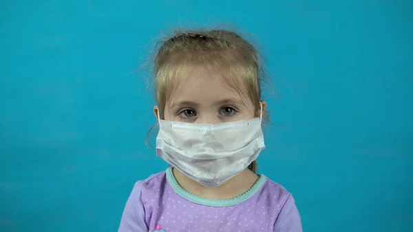 Fetiță într-o mască medicală pe un fundal albastru . — Fotografie, imagine de stoc