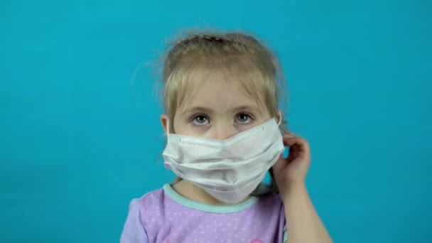 La bambina toglie una maschera medica su uno sfondo blu . — Video Stock