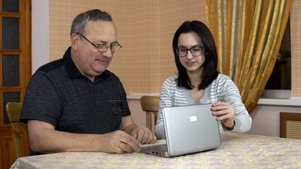 Daughter teaches father how to use a laptop. A young woman showed how to open a laptop to her old father. Family is sitting in a cozy room