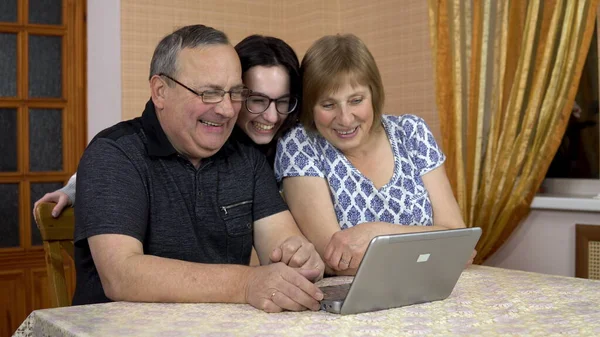 A man and a woman communicate with friends via video communication via a laptop. A young girl approached her parents and also began to communicate. The family is sitting in a comfortable room.