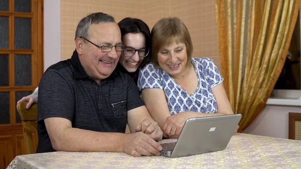 A man and a woman communicate with friends via video communication via a laptop. A young girl approached her parents and also began to communicate. The family is sitting in a comfortable room. — Stock Photo, Image