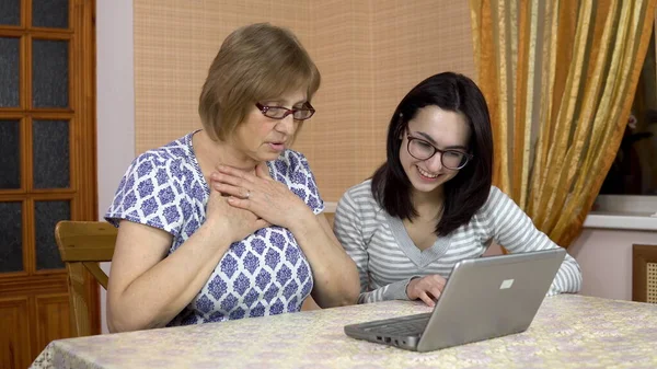 Daughter teaches mother how to use a laptop. A young woman showed how to open her old mothers laptop. The woman is surprised. The family is sitting in a comfortable room. — Stock Photo, Image