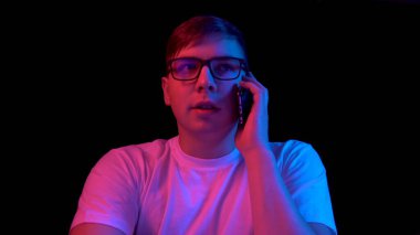 Young man with a phone. A man is talking on the phone. Blue and red light falls on a man on a black background.