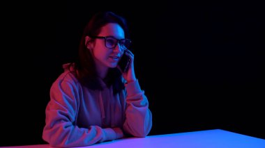 Young woman with a phone. A woman is talking on the phone. Blue and red light falls on a woman on a black background.
