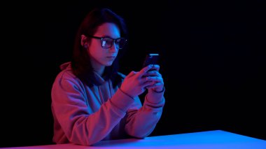 Young woman with a smartphone. Woman use the phone. Blue and red light falls on a woman on a black background.