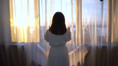 Beyaz önlüklü genç bir kadın pencereye doğru yürür ve perdeleri açar. Sabah kız pencereden dışarı bakar ve parlak güneş parlar..
