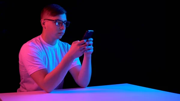 Giovanotto con uno smartphone. Un uomo sta usando un telefono. Luce blu e rossa cade su un uomo su uno sfondo nero . — Foto Stock
