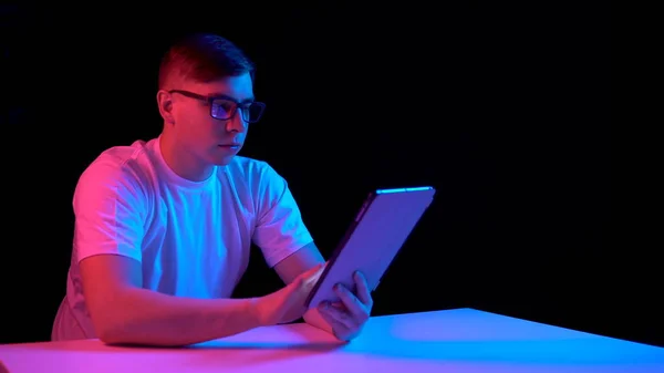 Young man with a tablet. A man is using a tablet. Blue and red light falls on a man on a black background. — 스톡 사진