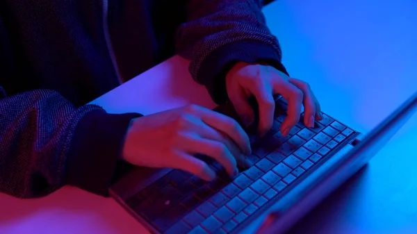 Une jeune femme tape sur un clavier d'ordinateur portable. Les mains en l'air. Un pirate pirate un ordinateur portable. Lumière bleue et rouge tombe sur les mains . — Photo