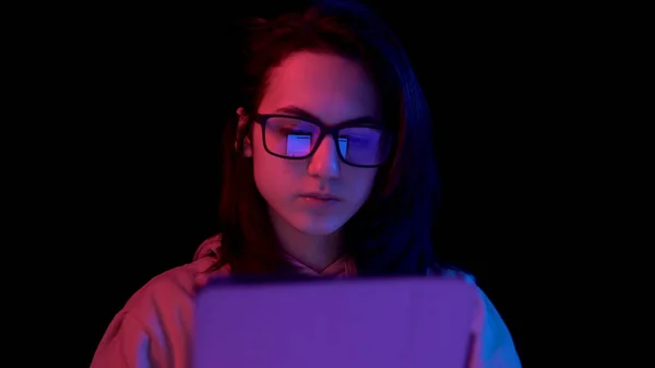 Uma jovem com um tablet. Uma mulher está a usar um tablet. Luz azul e vermelha cai sobre uma mulher em um fundo preto . — Fotografia de Stock