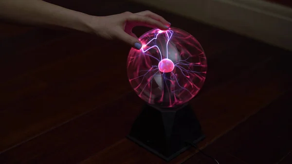 Una mano femenina toca una bola de plasma que emite pequeños rayos. Experimentos con electricidad en la oscuridad . — Foto de Stock