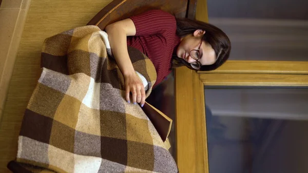 Una ragazza sta leggendo un libro. Una ragazza giace su un davanzale vicino alla finestra con un libro in mano. Fuori dalla serata. Foto verticale . — Foto Stock