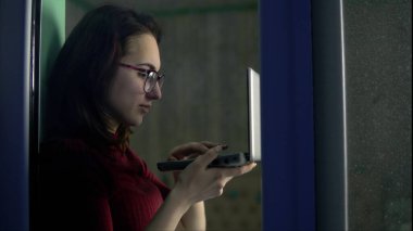 Genç bir kadın elinde dizüstü bilgisayarla evde oturuyor. Bir kız pencere pervazına oturur ve dizüstü bilgisayarla çalışır. Camın arkasına bak..