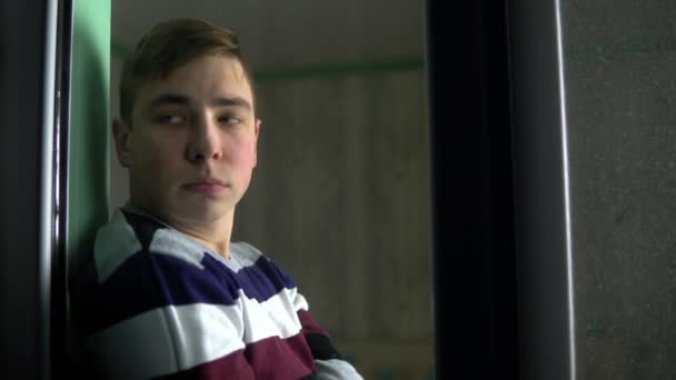 Smutný mladík sedí doma v karanténě. Muž sedí na parapetu a dívá se z okna. Pohled za sklo. — Stock video