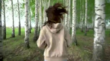 Genç bir kadın huş ağacından geçiyor. Kız ağaçların arasında koşuyor. Arka plan.