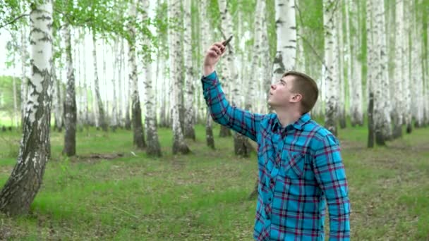 En ung man söker ett mobilt nätverk i en björkskog. En man pratar i telefon, men kopplingen är avbruten. Han är nervös.. — Stockvideo