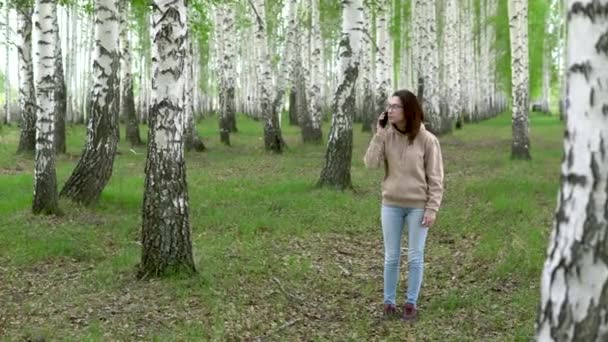 Une jeune femme cherche un réseau cellulaire dans une forêt de bouleaux. Une fille parle au téléphone, mais la connexion est interrompue. La femme est nerveuse. — Video