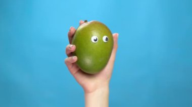 Mango, kadının elinde gözleri olan yakın plan. Mango mavi bir arka planda gözleri titretir ve döndürür. Yavaş çekim.