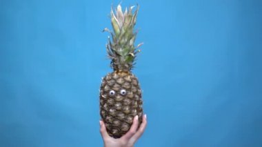 Ananaslı ve eli kadın eli yakın. Patatesler mavi arka planda sallanır ve gözleri büker. Yavaş çekim.