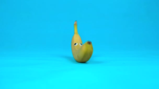 Banana com os olhos rola lentamente. Banana com rolos em um fundo azul. Movimento lento . — Vídeo de Stock