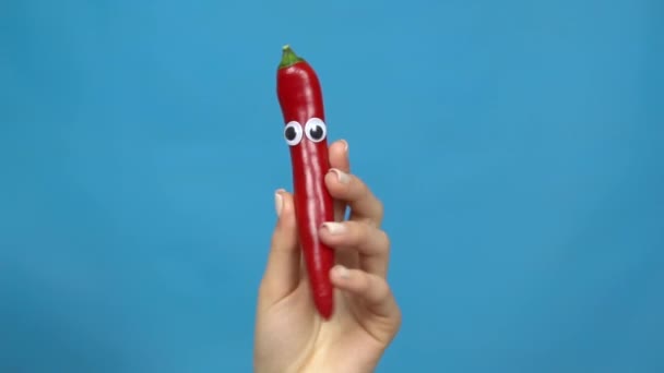 Chilli paprikové oči v ženské ruce zblízka. Chilli paprika se třese a kroutí očima na modrém pozadí. Zpomalený pohyb. — Stock video