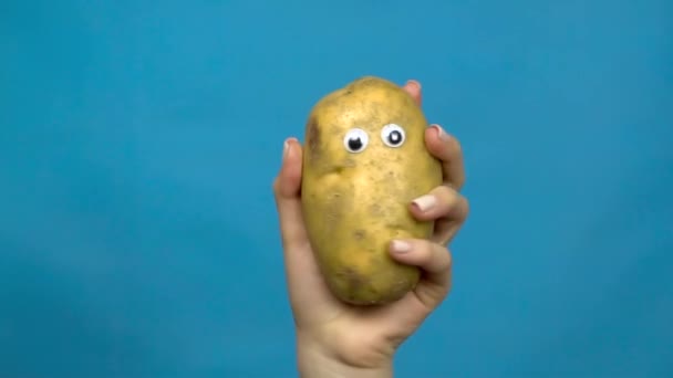Potato with eyes in a woman hand close-up. Potatoes shakes and twists eyes on a blue background. Slow motion. — Stock Video