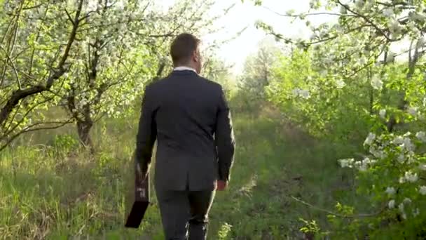 Un uomo d'affari cammina nel meleto e si guarda intorno. Un uomo in giacca e cravatta guarda i suoi beni. Un uomo nella natura. — Video Stock