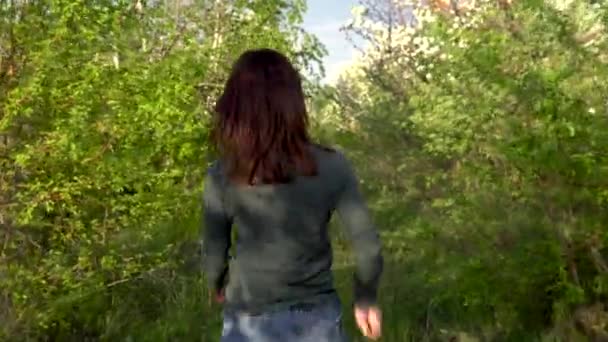 Uma jovem caminha entre macieiras. Uma menina caminha através de um jardim florido. Visão traseira . — Vídeo de Stock