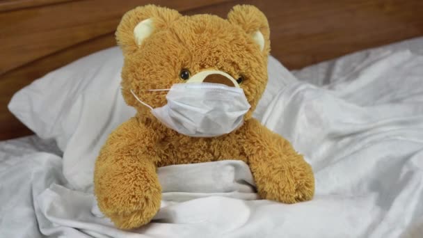Een teddybeer meet de temperatuur met een kwikthermometer. De dokter zet een thermometer op de beer. De beer ligt in bed met een medisch masker.. — Stockvideo