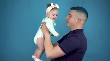 Mavi saçlı genç bir baba kucağında bir bebek tutuyor. Çocuklu alternatif adam mavi arka plandaki kameraya bak..
