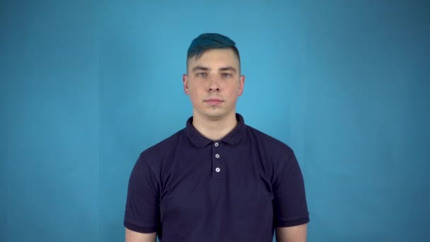 Een jonge man met blauw haar houdt kleurrijke opblaasbare ballen in zijn handen. Alternatieve man glimlacht met ballen op een blauwe achtergrond. — Stockvideo