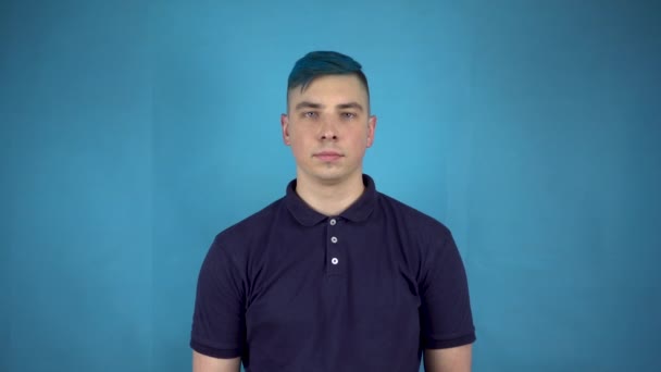 Un hombre joven con el pelo azul sostiene en sus manos bolas inflables coloridas. Hombre alternativo sonríe con bolas sobre un fondo azul. — Vídeos de Stock