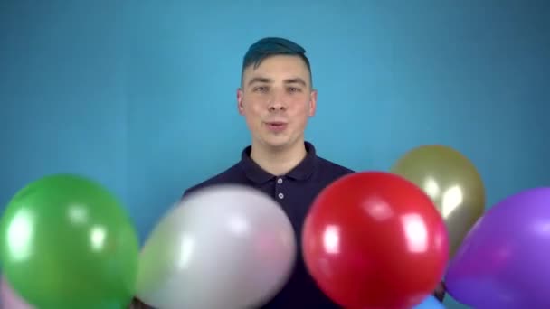 Un hombre joven con el pelo azul sostiene en sus manos bolas inflables coloridas. Persona alternativa que se divierte con bolas sobre un fondo azul. — Vídeos de Stock