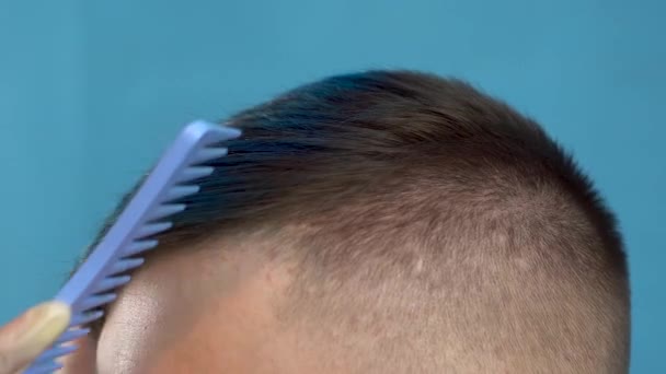 Молодой человек с голубыми волосами расчесывает волосы. Альтернативный мужчина в салоне красоты на синем фоне . — стоковое видео