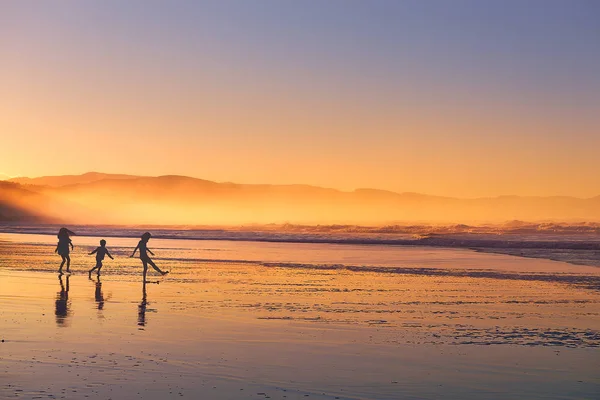 Barn siluett spela och ha kul på stranden vid solnedgången — Stockfoto