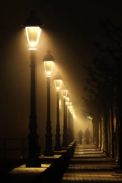 Coppia che cammina su strada buia illuminata con lampioni — Foto Stock