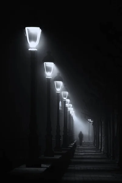 Людина, що йде по темній вулиці, освітлена вуличними ліхтарями — стокове фото
