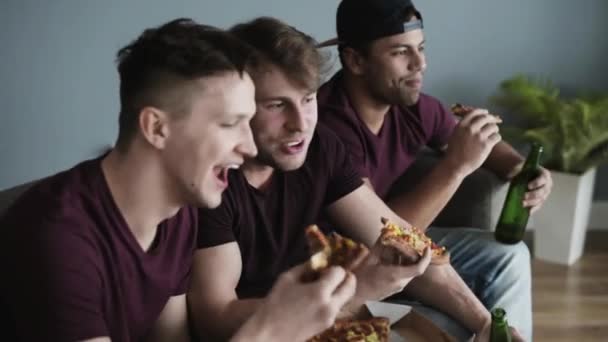 Chicos tomando pizza y cervezas mientras compiten en deportes — Vídeo de stock