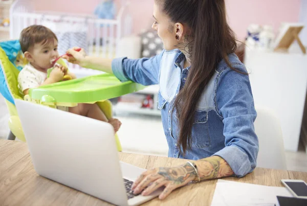 Mamma arbetar på laptop och utfodring baby — Stockfoto