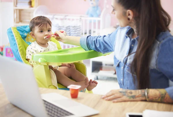 Mamma arbetar på laptop och utfodring baby — Stockfoto