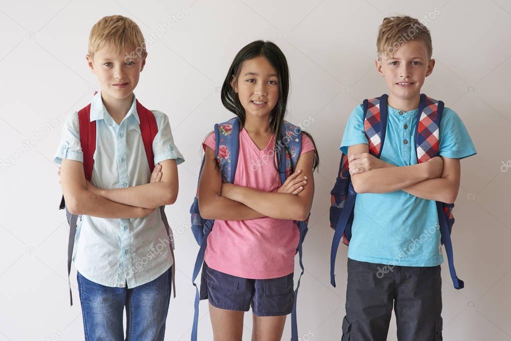 pupils with backpacks standing with arms crossed